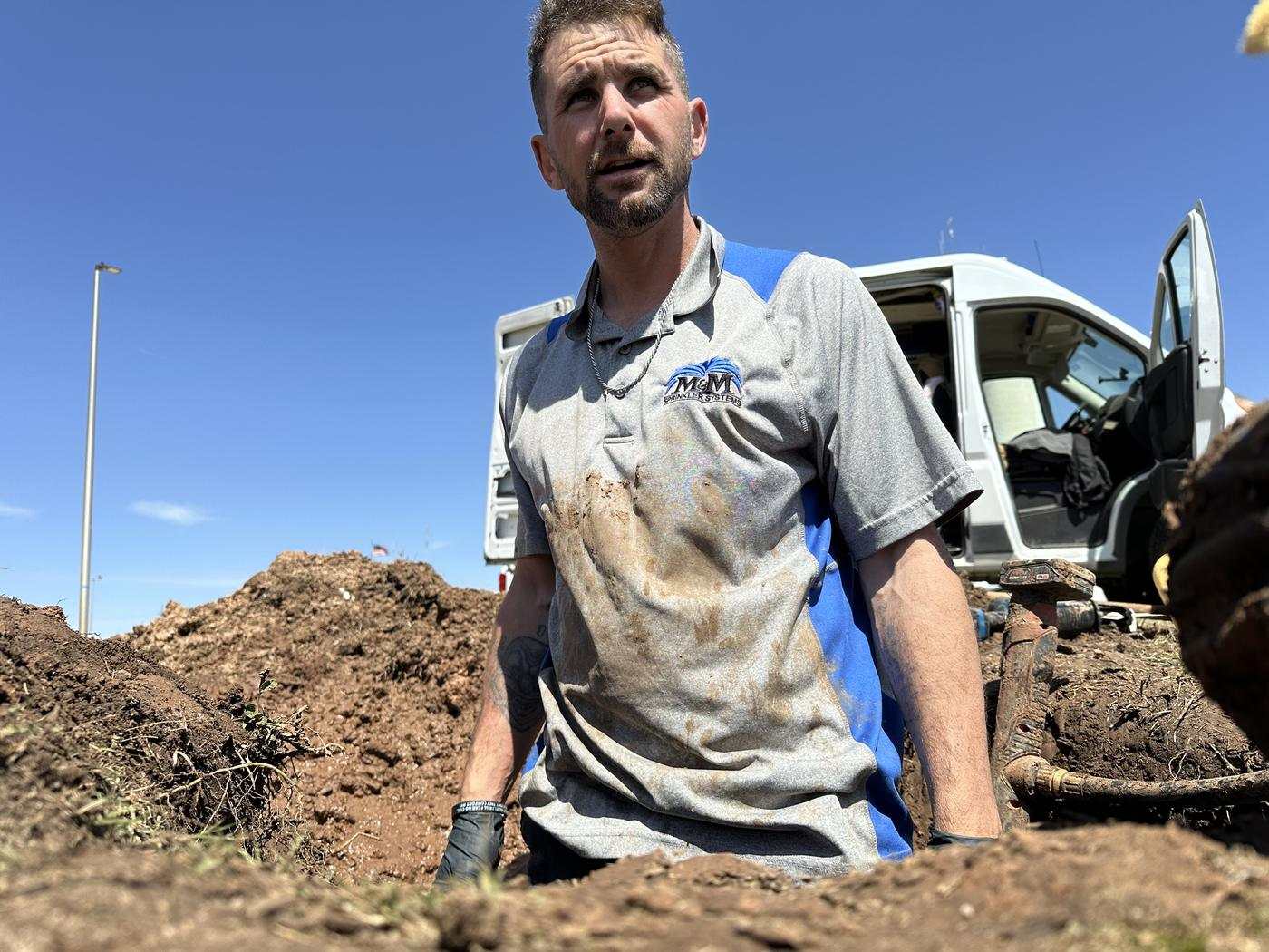 M&M technician standing in a dug-out trench beside the work truck
